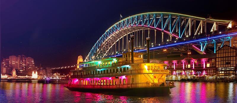 The Showboat Vivid Sydney cruise gliding past the Harbour Bridge