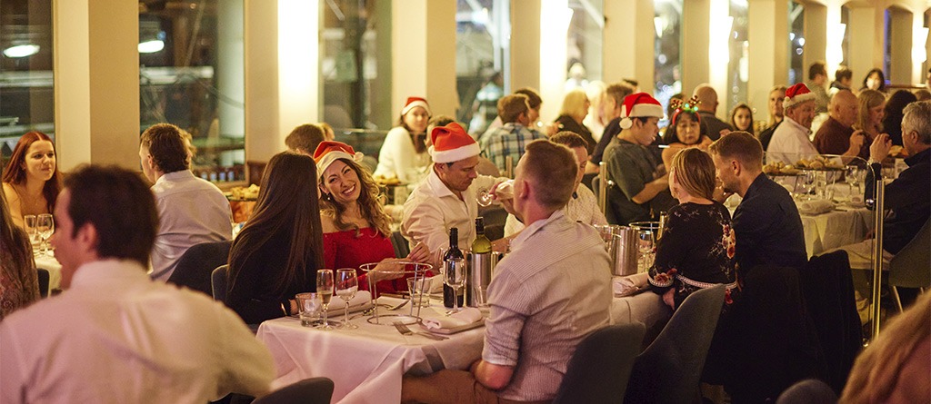 Guests dining and celebrating in Santa hats aboard the Showboat Christmas party dinner cruise in Sydney