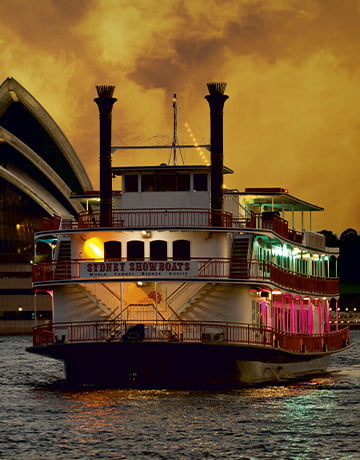 The authentic paddlewheeler cruising past the Opera House under the golden sky.
